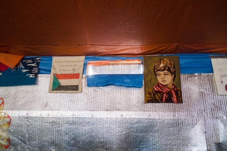 Au mur un drapeau du Soudan et une tapisserie chelou