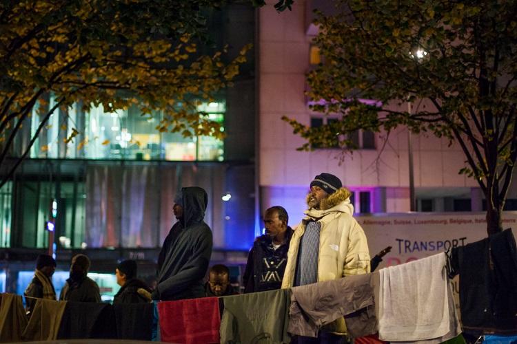 Plusieurs réfugiés regardent la manifestation de loin