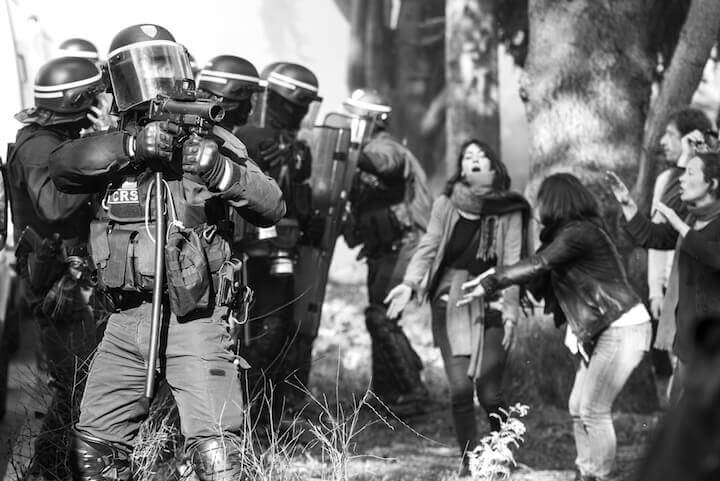 Un CRS vise avec un LBD40 un manifestant, au milieu de badauds nassés. Jour d'une manifestation en soutien aux cheminots, à la fonction publique et contre les expulsions en cours sur la ZAD. 14 avril 2018.