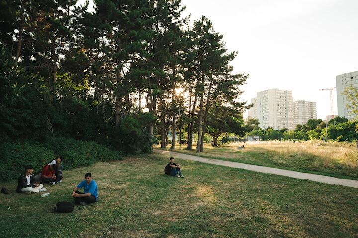 Des Afghans attendent sur l'herbe du parc de la Bergère, derrière la forêt avec le campement.