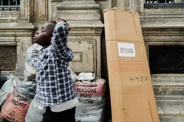 Sur le parvis de l'Hôtel de Ville, les familles attendent assises sur des cartons et se nourrissent grâce aux associations