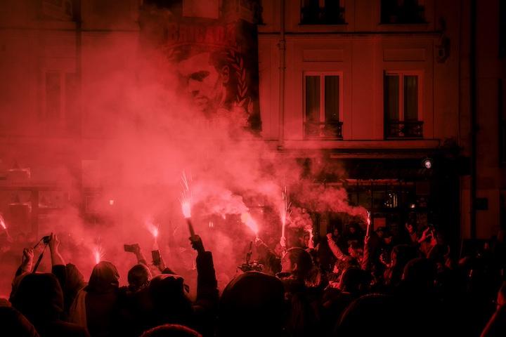 Les lancers de fumigènes s’enchaînent, et recouvrent la place d’une fumée rouge étouffante, pendant qu’une banderole en l’honneur du patron est déployée au-dessus du bar