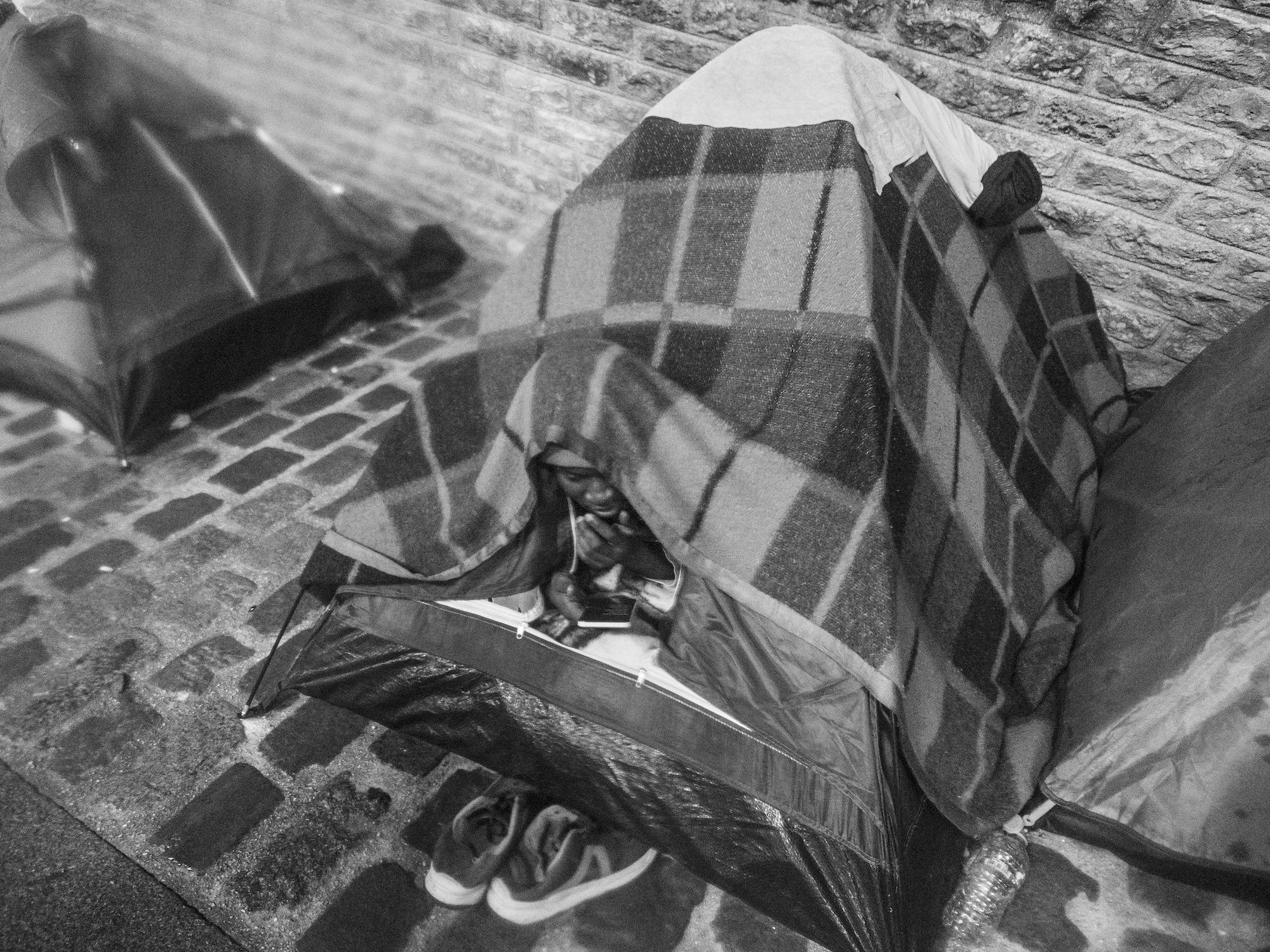 Chérif, smartphone dans les mains, regarde le match de foot depuis sa tente sous le Pont de Sully