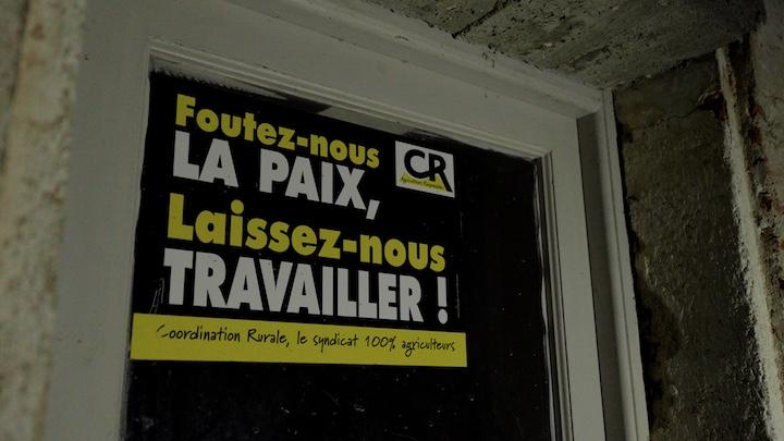 Une affiche « Foutez-nous la paix, Laissez-nous travailler ! » de la Coordination rurale (CR) est collée au mur qui mène aux toilettes extérieures en piteux état.