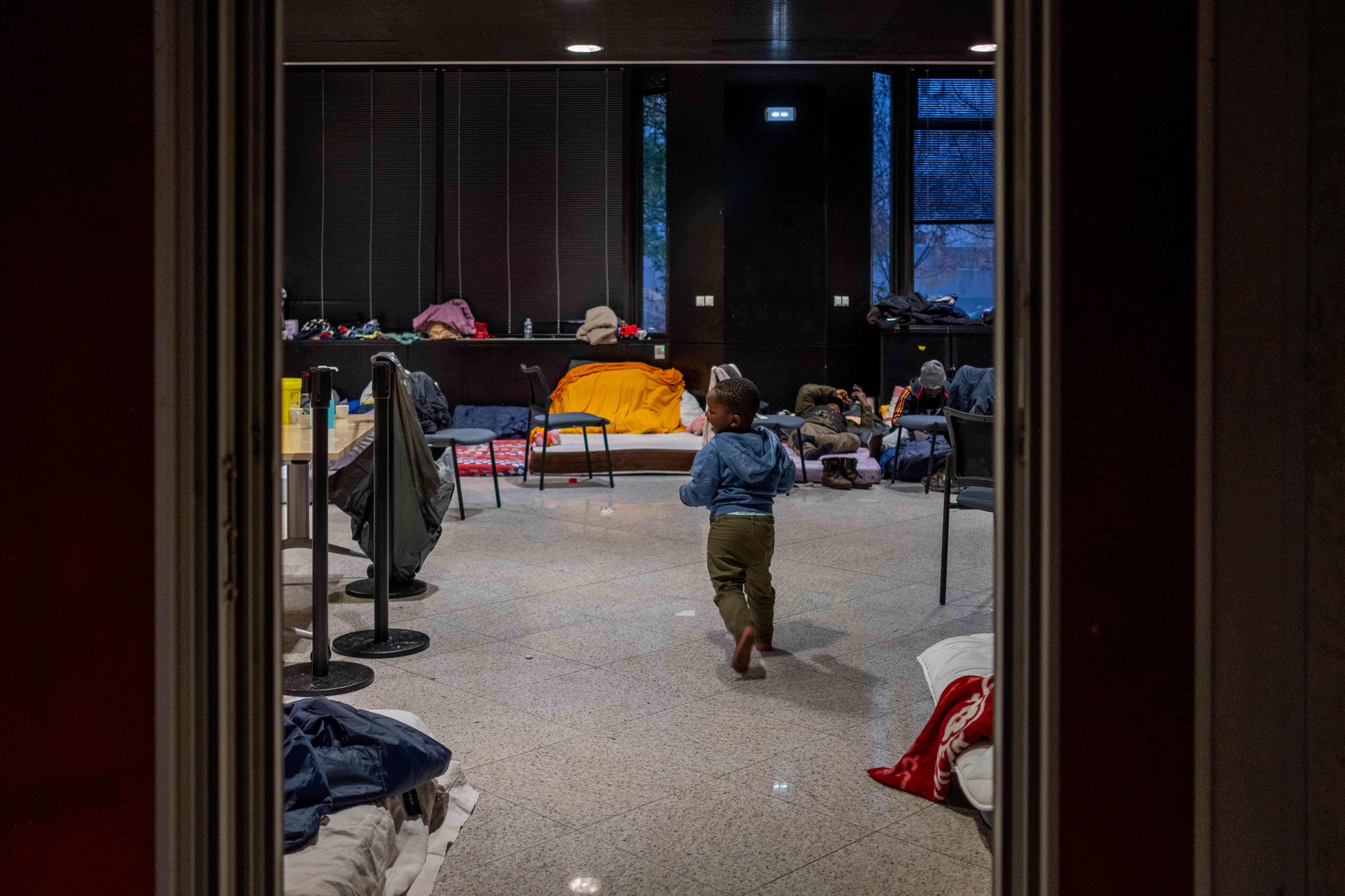 Dans le dortoir improvisé au siège de la Métropole de Grenoble, de nombreux enfants en bas âge crient et jouent en sautant sur des matelas de fortune